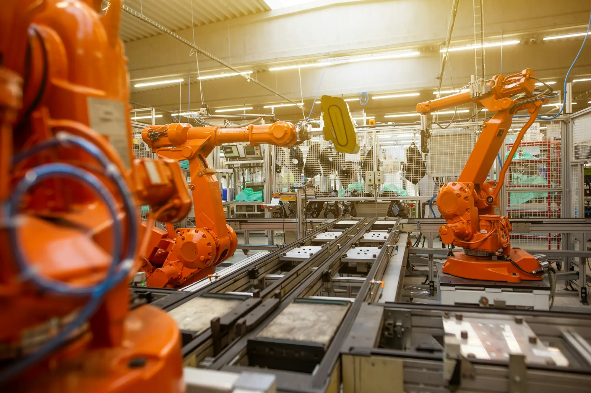 Roboty przemysłowe nad przenośnikiem paletowym w hali produkcyjnej