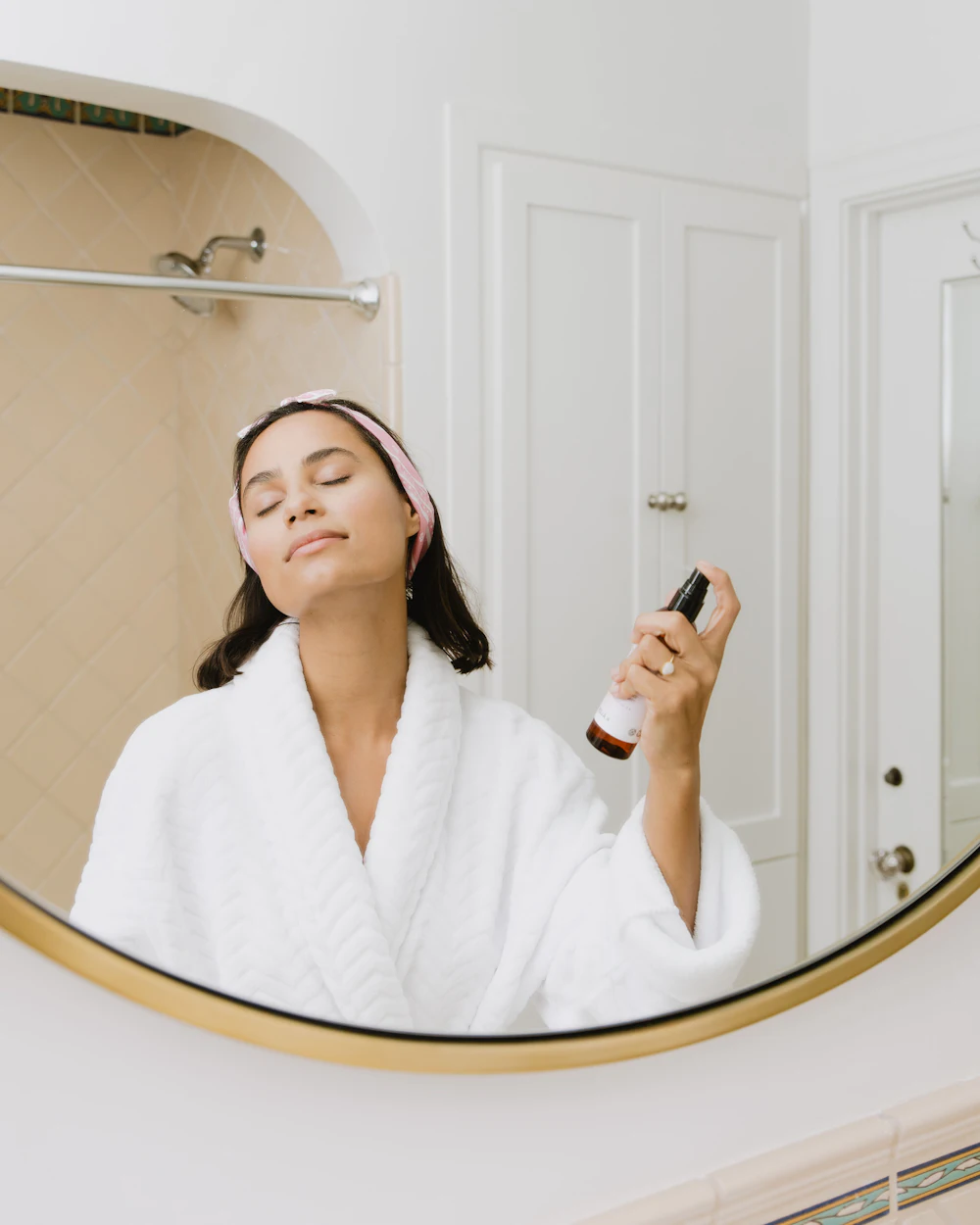 Kobieta w szlafroku nakłada serum przed lustrem